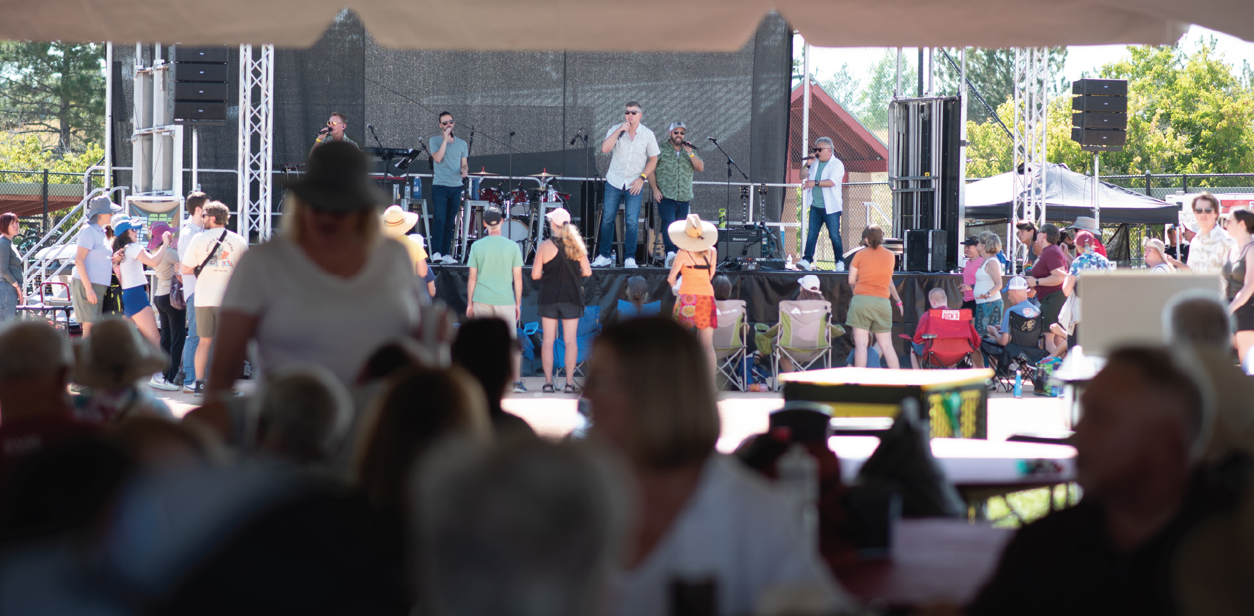 Band playing in the background while people eat in the shaded tent in the foreground. 