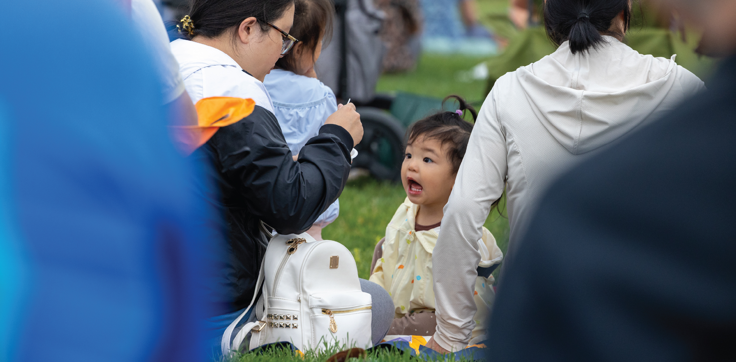 Child being feed surrounded by family enjoying the music on a picnic blanket.