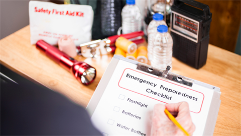 A hand holding a pencil checks off items on an emergency preparedness list