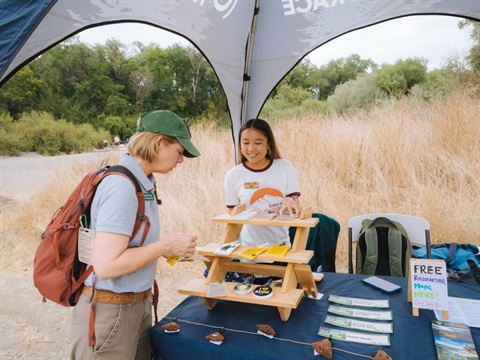 two leave no trace volunteers discuss pamphlets and stickers on top of a picnic table