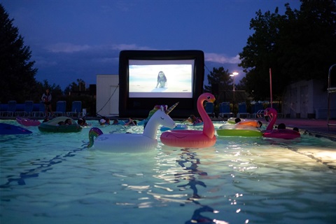 Giant unicorn & flamingo inflatable floating amongst others in the north pool at night with movie night screen in the background other 
